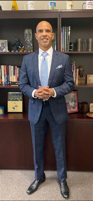 Principal Church in a blue suit in front of shelves in his office